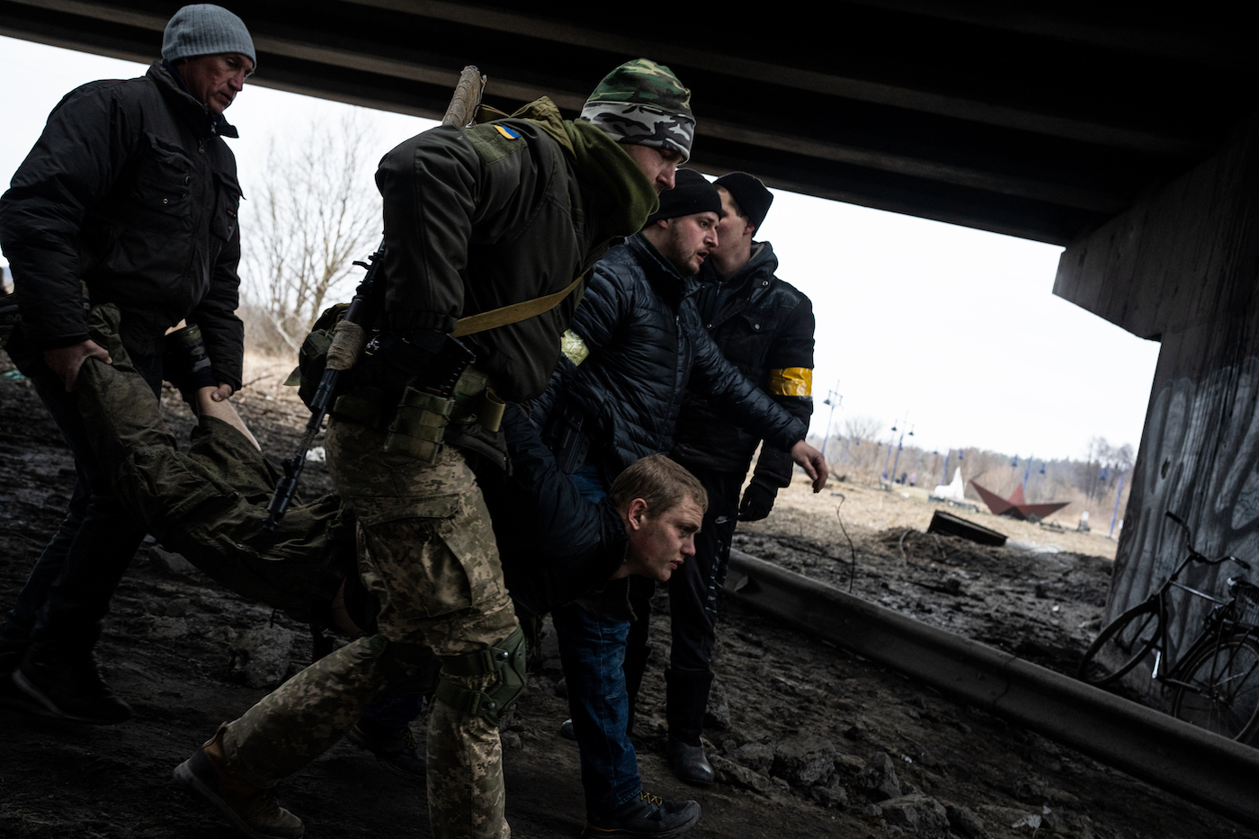 Ukrainian Territorial Defense members carry a Russian POW across the destroyed bridge on the Irpin River in Irpin, Ukraine on March 5, 2022 Wolfgang Schwan - Anadolu Agency